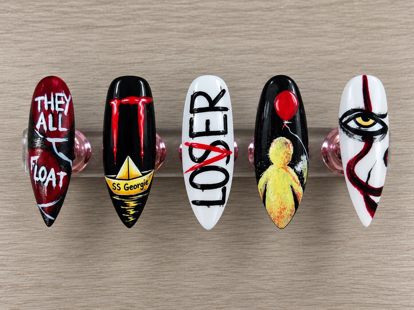 Pennywise inspired horror nail art with a red balloon yellow raincoat paper boat and hand painted details displayed upright on clear stands